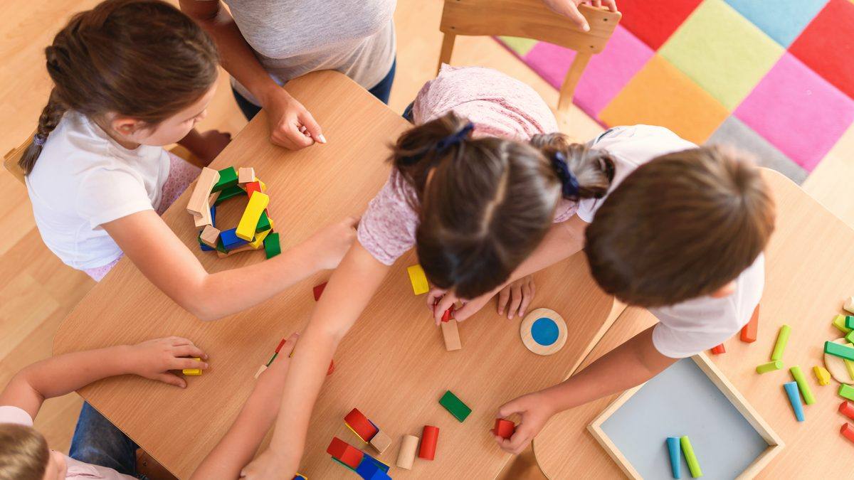 Professionnelle de la petite enfance et jeunes enfants autour d'une table de jeux en bois dans une salle de crèche