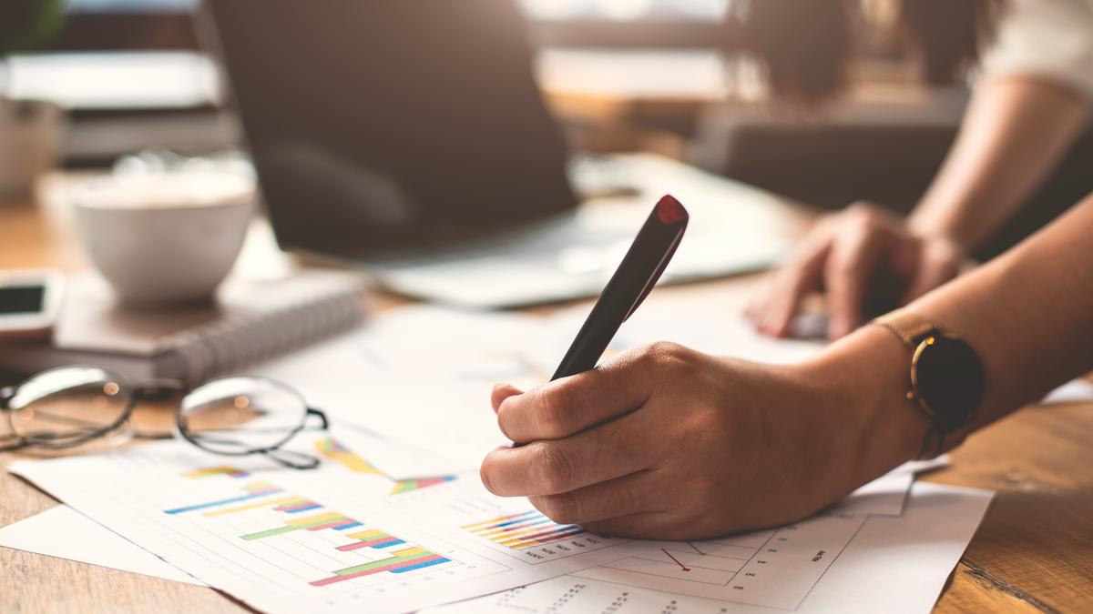 Main de femme écrivant sur des documents posés sur un bureau en bois, dans une lumière chaude
