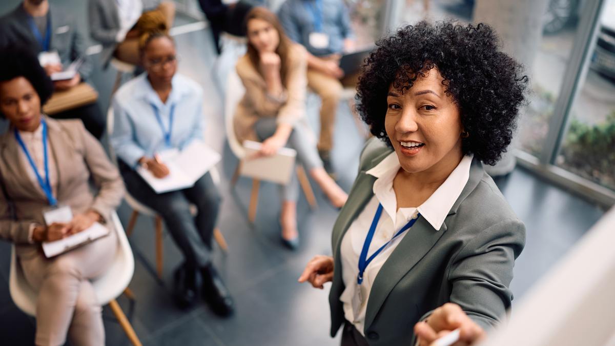 Femme debout présentant son parcours devant un groupe de personnes assises qui prennent des notes