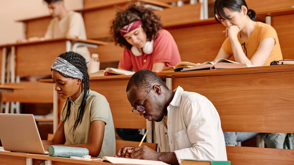 Étudiants et étudiantes assis sur les gradins en bois d'un amphithéâtre, penchés sur leurs cahiers et un ordinateur portable