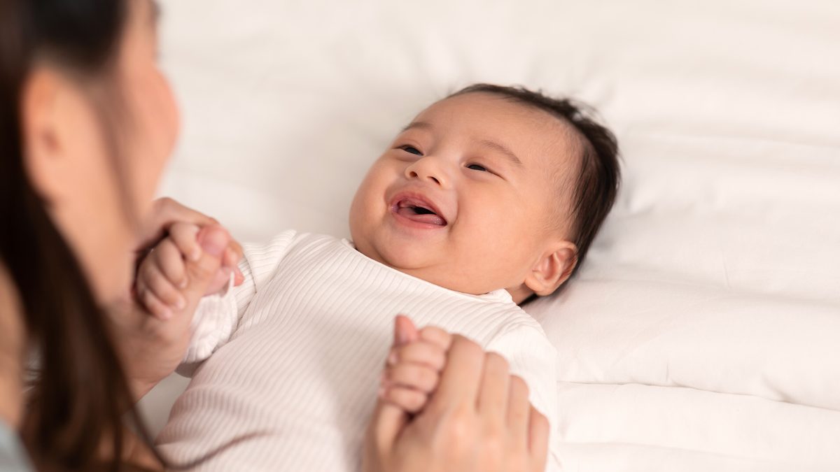 Une jeune maman sourit et parle à son nouveau-né allongé sur un lit en lui tenant les mains