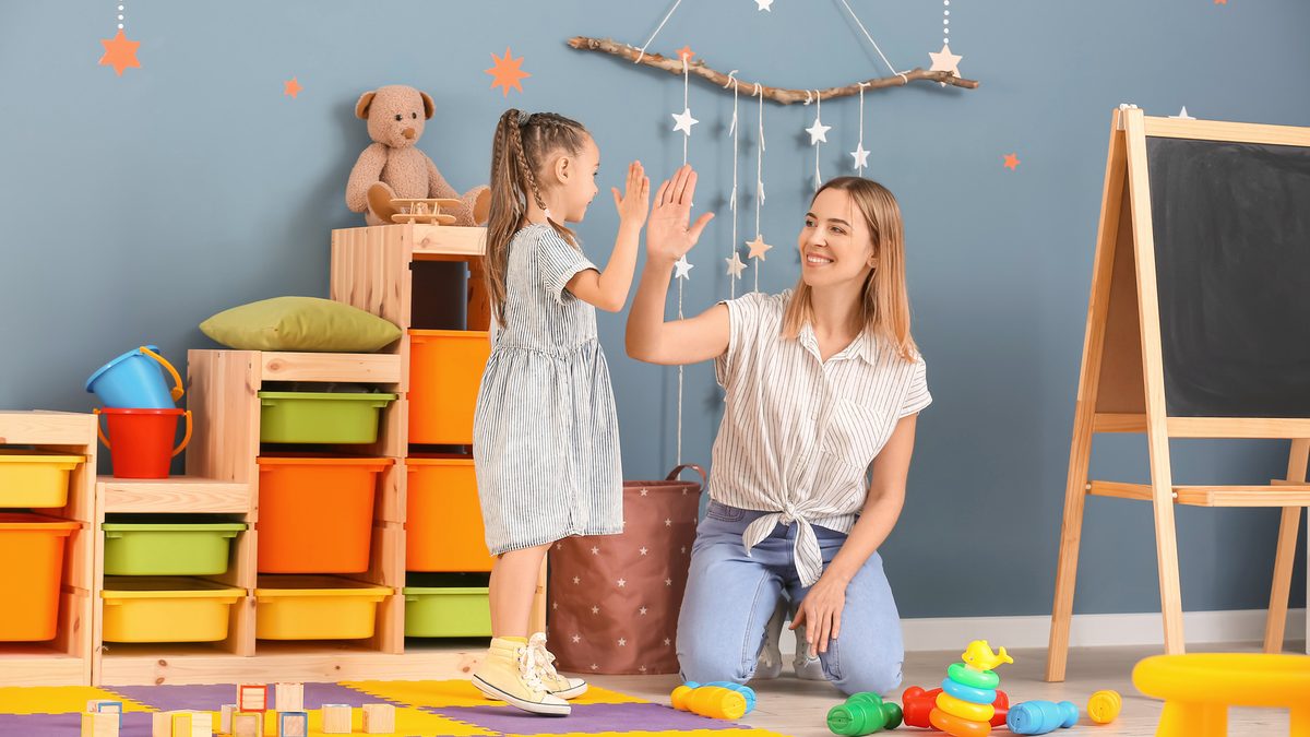 Une jeune professionnelle souriante tape dans la main d'une petite fille, dans une chambre d'enfant colorée