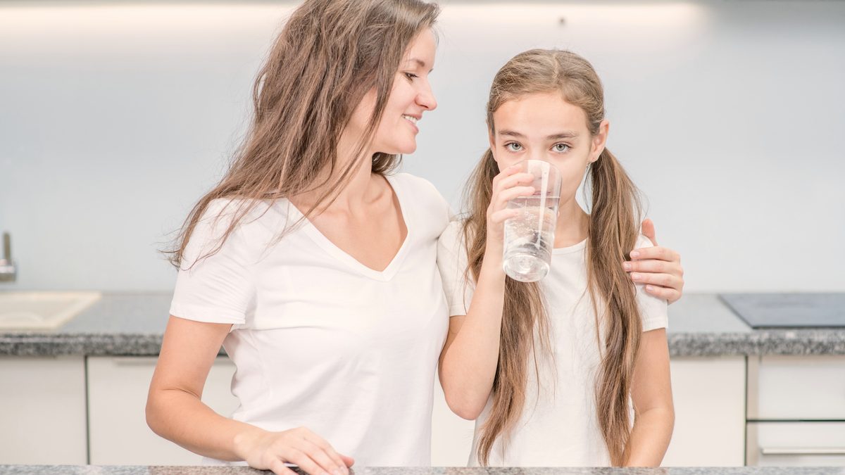 Une mère et sa fille, un verre d'eau à la main, dans la cuisine