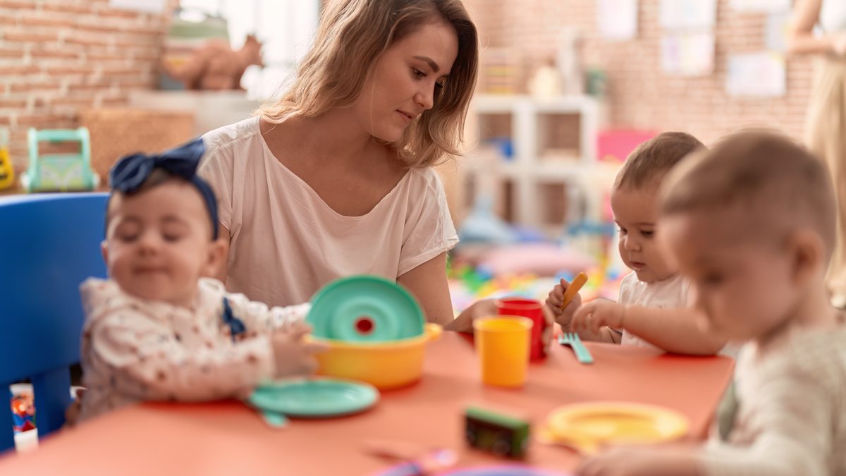 Professionnelle de crèche accompagnant plusieurs jeunes enfants pendant le repas à table