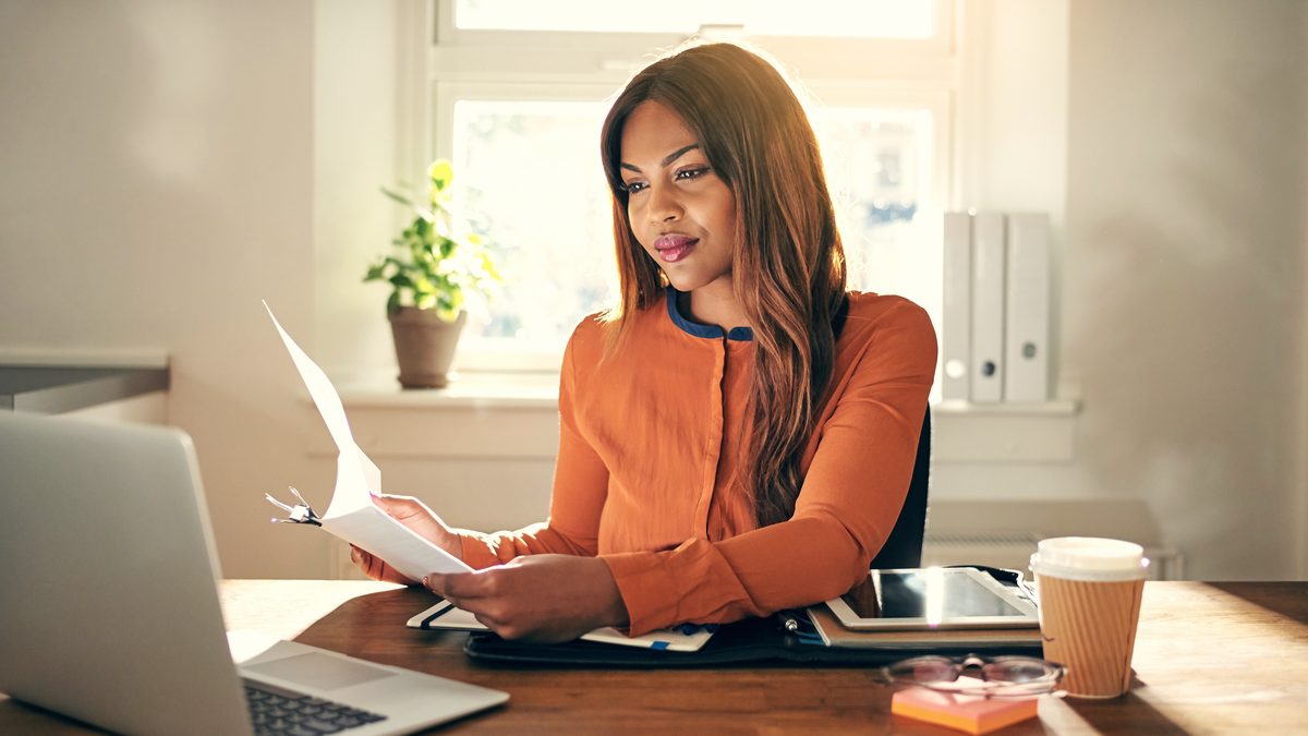 Une professionnelle relit attentivement un document papier à son bureau, devant son ordinateur portable