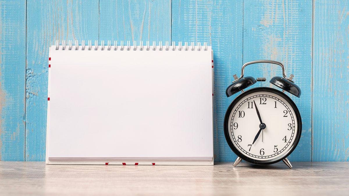 R&eacute;veil et carnet de notes pos&eacute;s sur une table en bois, &eacute;voquant l'organisation d'un planning de travail