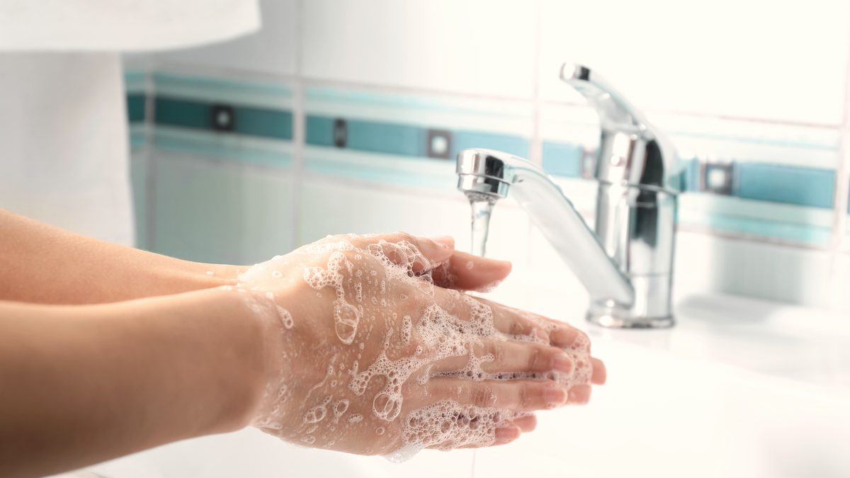 Une femme se lave les mains avec du savon sous un robinet