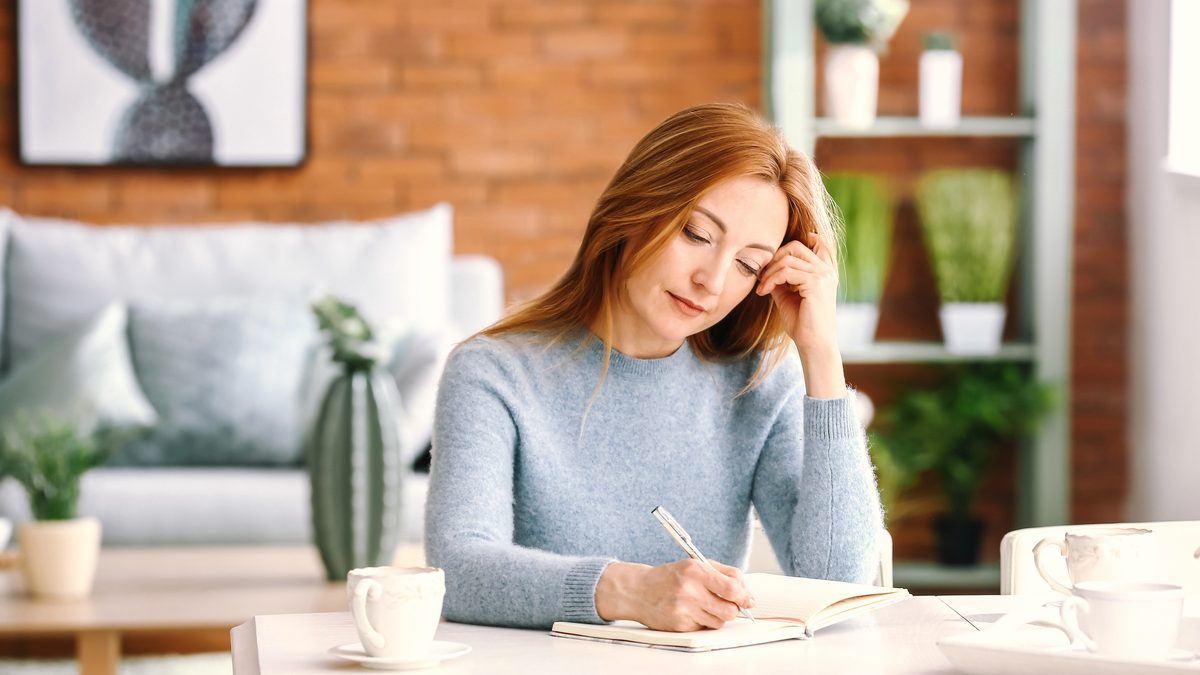 Femme adulte assise à une table, en train d'écrire dans un carnet chez elle