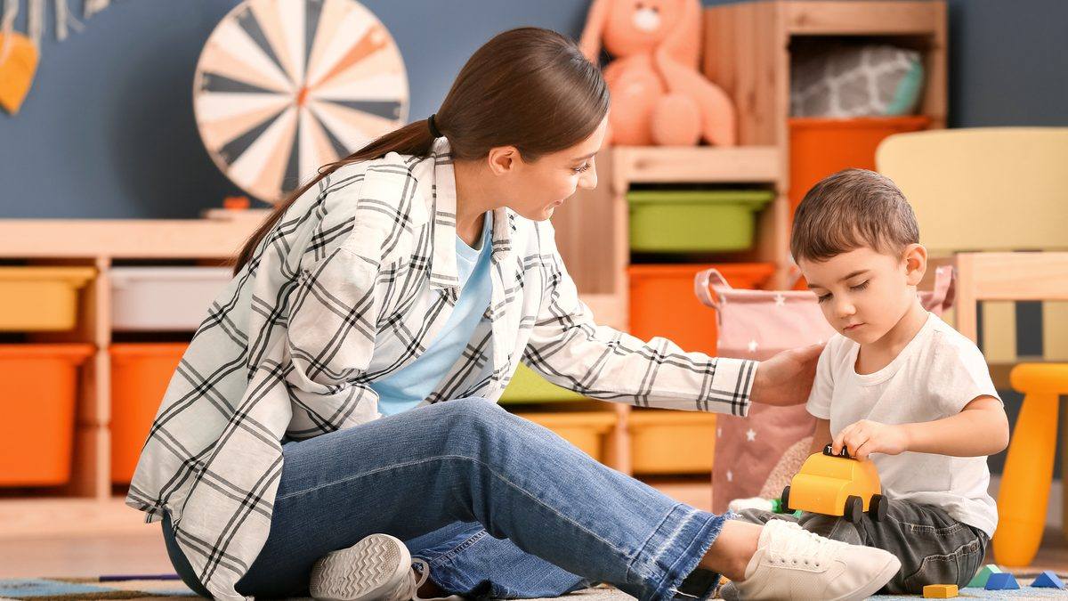 Professionnelle de la petite enfance jouant avec un jeune enfant dans un salon au domicile de la famille