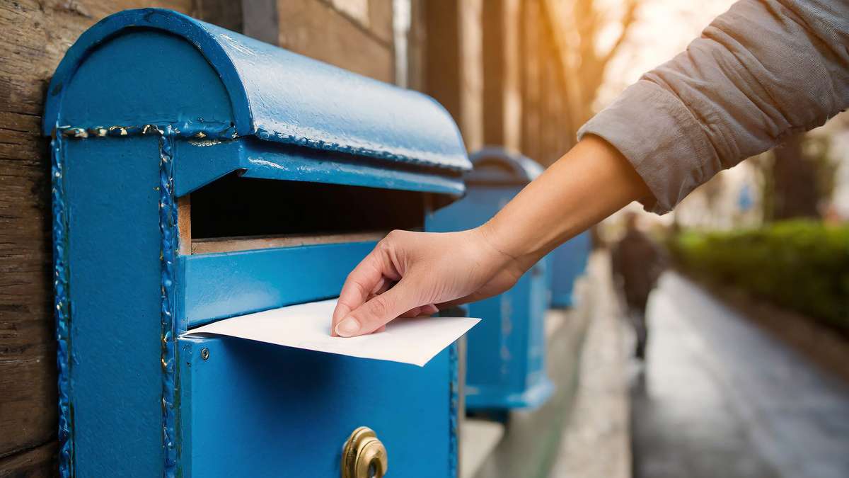 Main déposant une enveloppe de candidature dans une boîte aux lettres bleue dans une rue