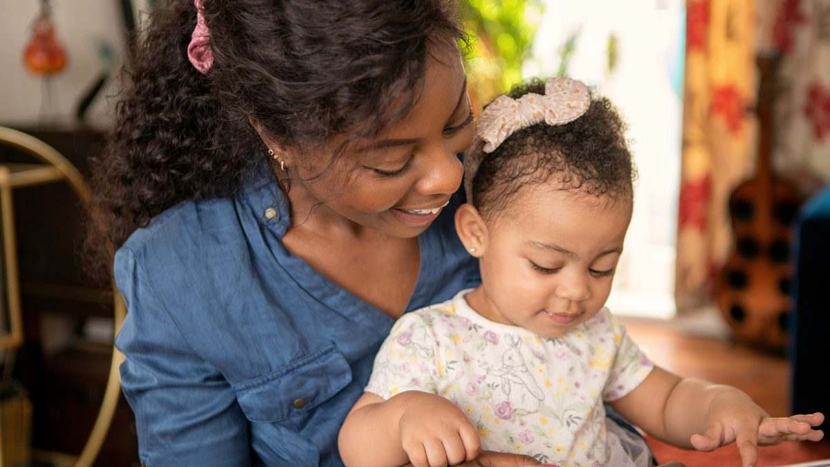 Une mère regarde un livre d'images avec sa petite fille assise sur ses genoux, moment d'échange favorisant le langage