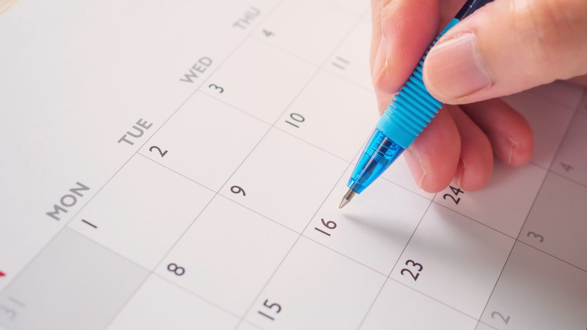 Main tenant un stylo et pointant une date entourée sur un calendrier