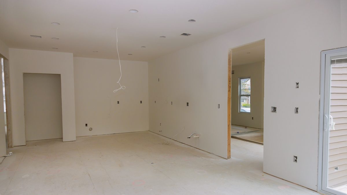 Une pièce vide en cours de rénovation, murs en plaques de plâtre et câblage électrique apparent, prête à être aménagée