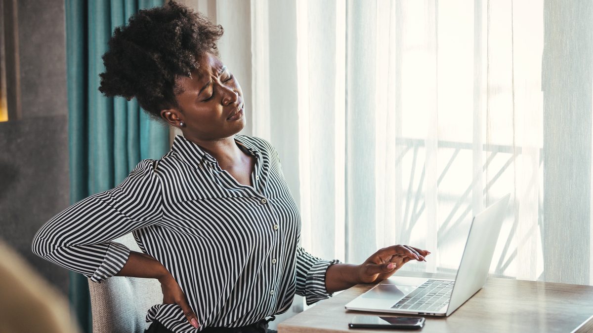 Une salariée se tient le bas du dos, assise à son bureau
