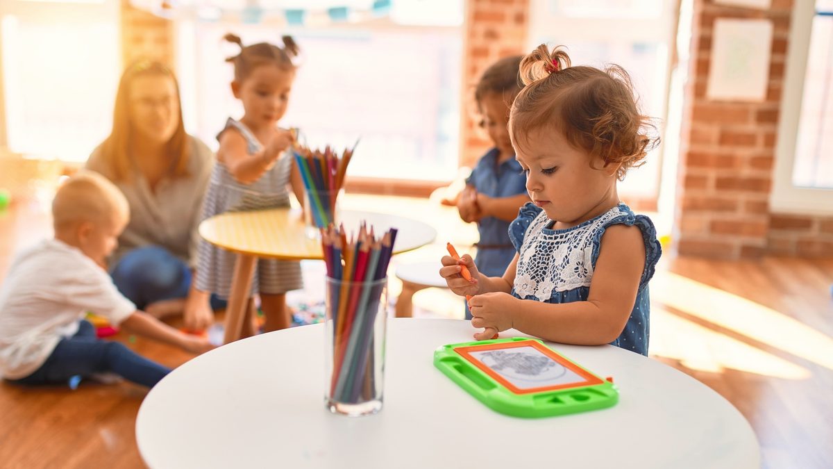 Une professionnelle et un petit groupe de tout-petits jouent et dessinent autour d'une table dans une salle lumineuse