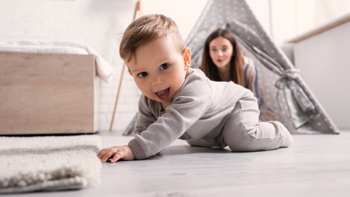 Bébé se déplaçant à quatre pattes sur le sol, sa mère assise en retrait