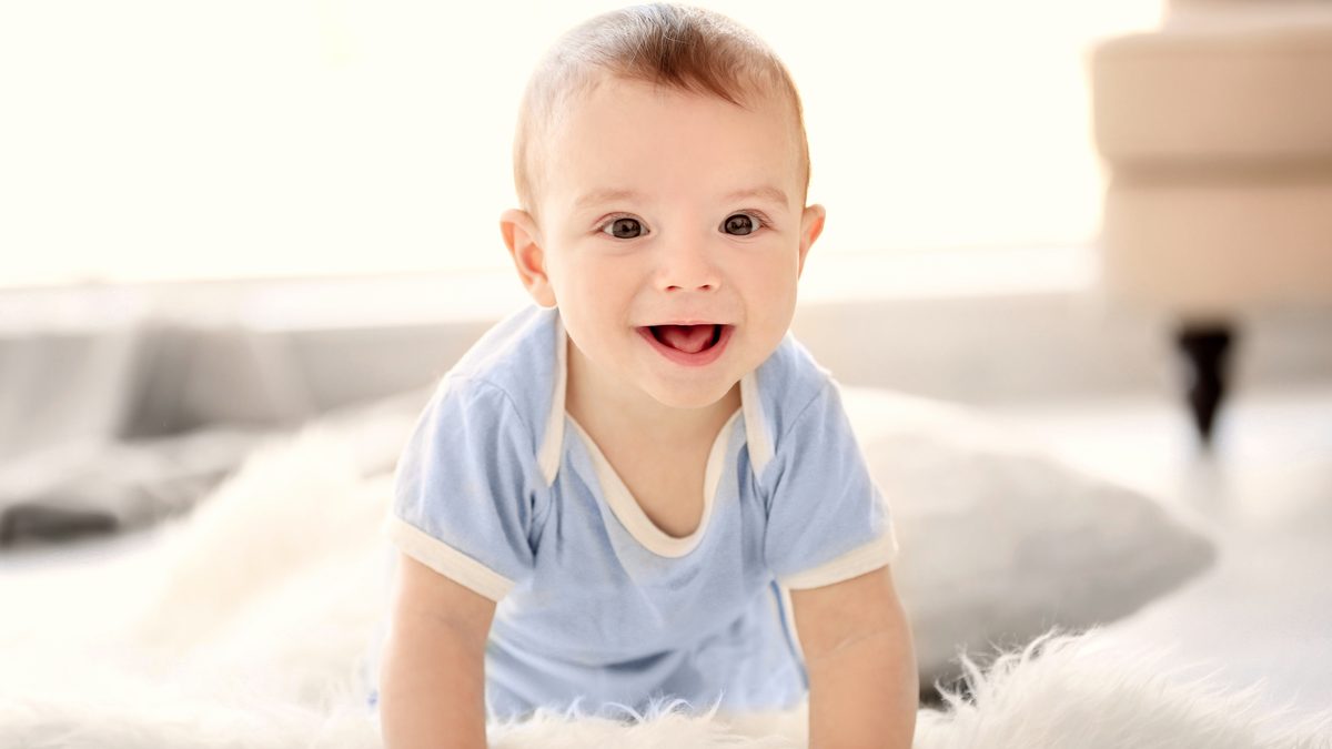 Bébé souriant à quatre pattes sur un tapis clair, libre de ses mouvements au sol