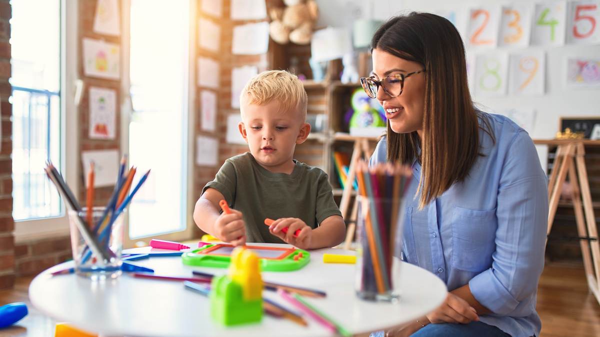 Une professionnelle de la petite enfance accompagne un jeune enfant qui dessine, seule avec lui dans une salle d'accueil