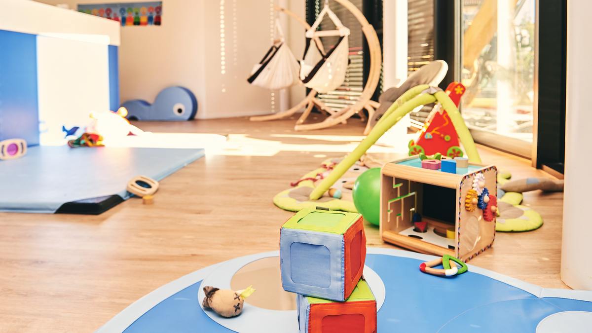 Salle de vie lumineuse d'une micro-crèche avec jeux en bois, tapis et mobilier bas