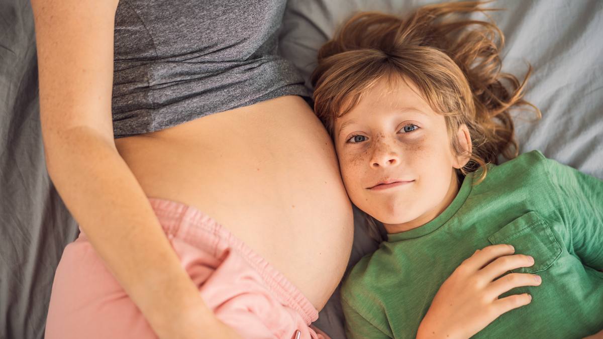 Jeune enfant posant l'oreille contre le ventre arrondi de sa mère, allongés côte à côte