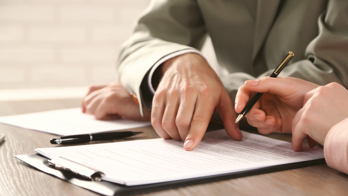 Mains d'une personne posées sur un dossier de documents administratifs, stylo à la main