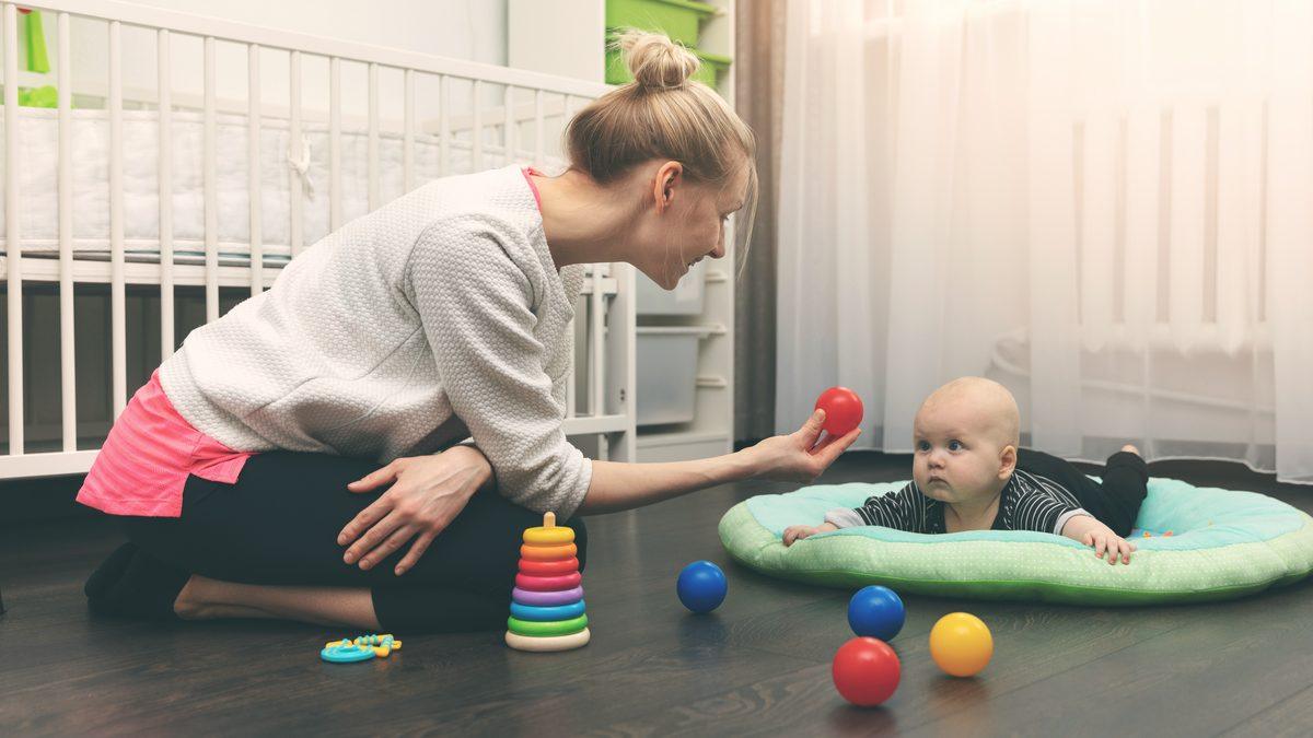Professionnelle penchée vers un bébé installé sur un tapis d'éveil dans une salle de crèche lumineuse