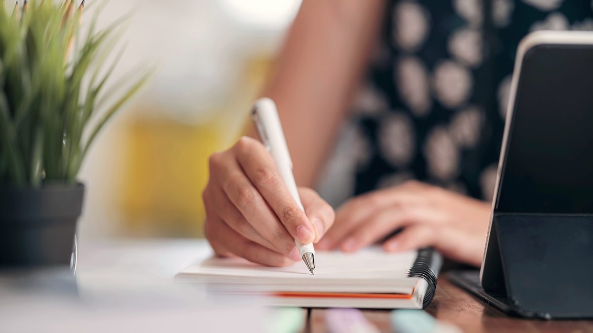 Mains d'une professionnelle prenant des notes dans un carnet posé sur une table