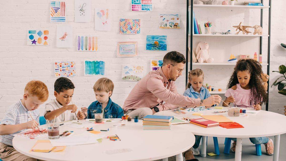Professionnel de la petite enfance accompagnant un groupe d'enfants autour d'une table d'activités de dessin