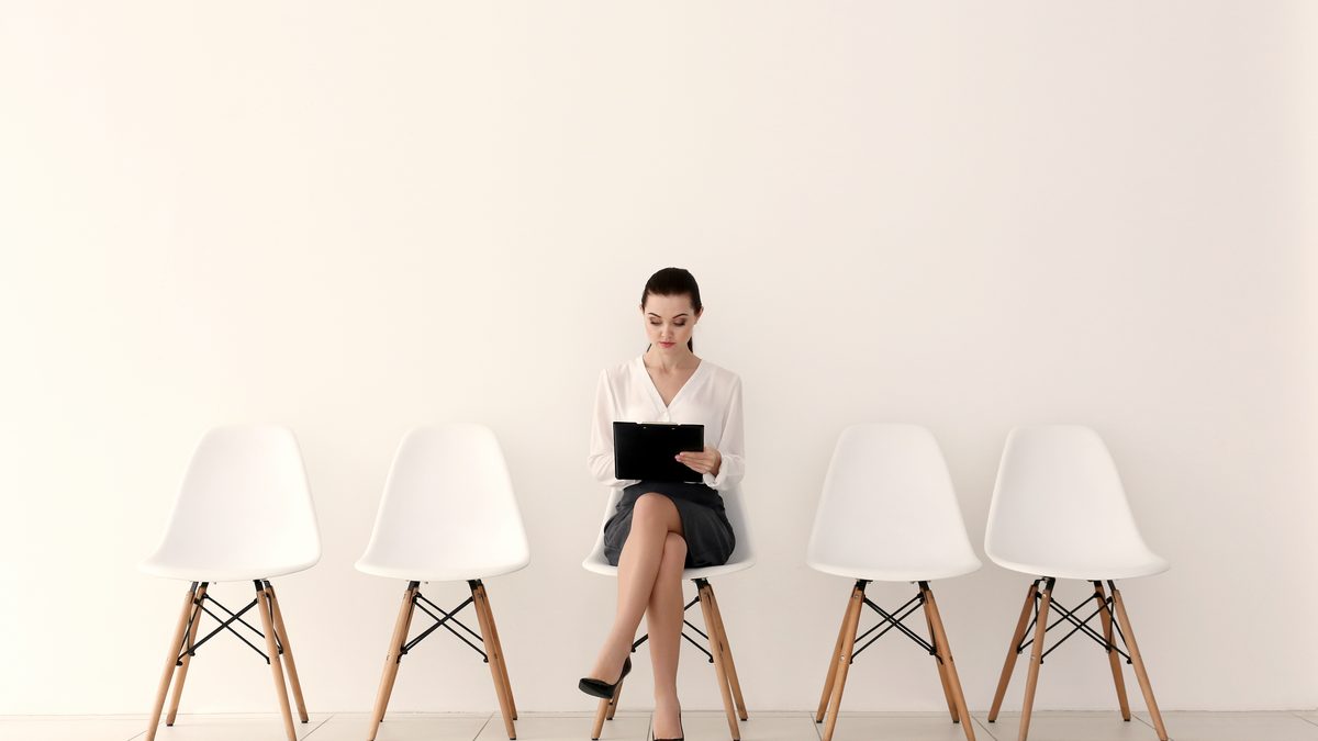 Jeune femme assise seule sur une rangée de chaises blanches, relisant un document avant son passage