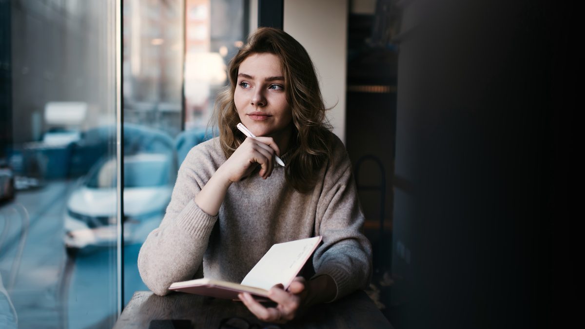 Jeune femme en formation, carnet à la main, prenant un temps de recul près d'une fenêtre