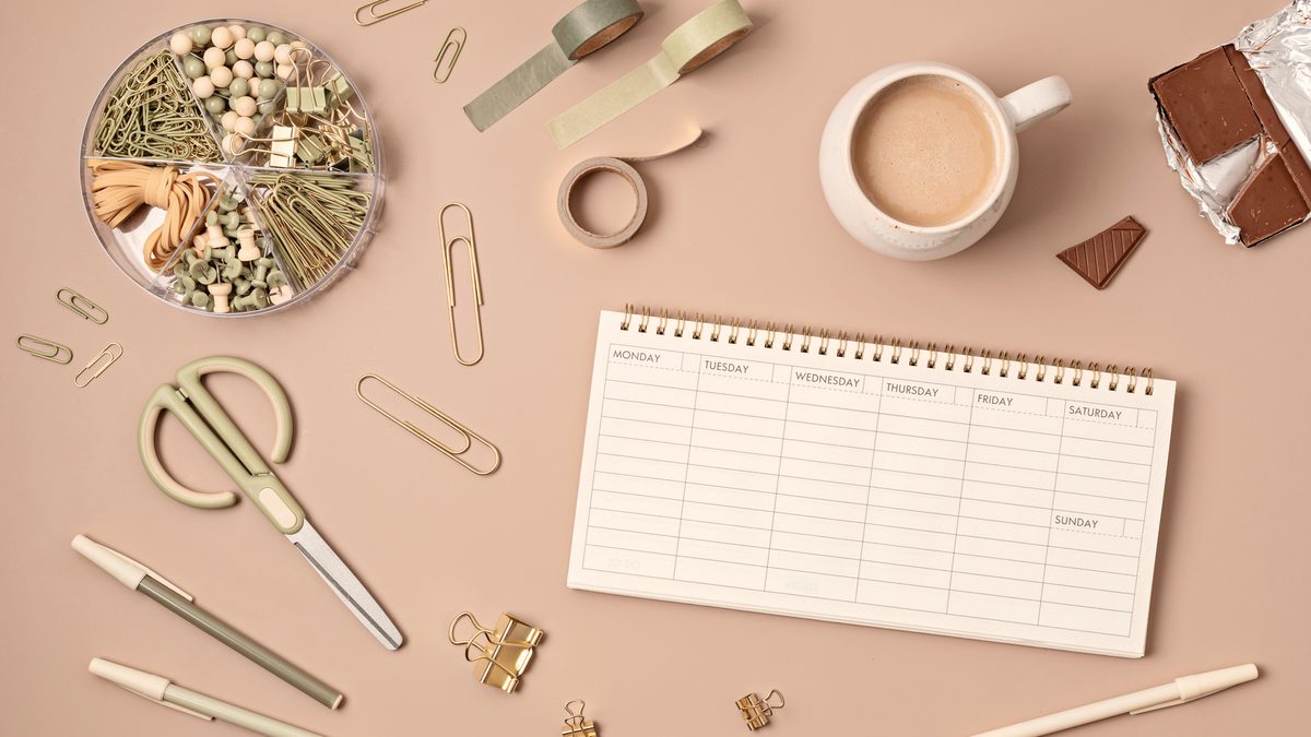 Un planning hebdomadaire et du matériel de papeterie posés à plat sur un bureau beige