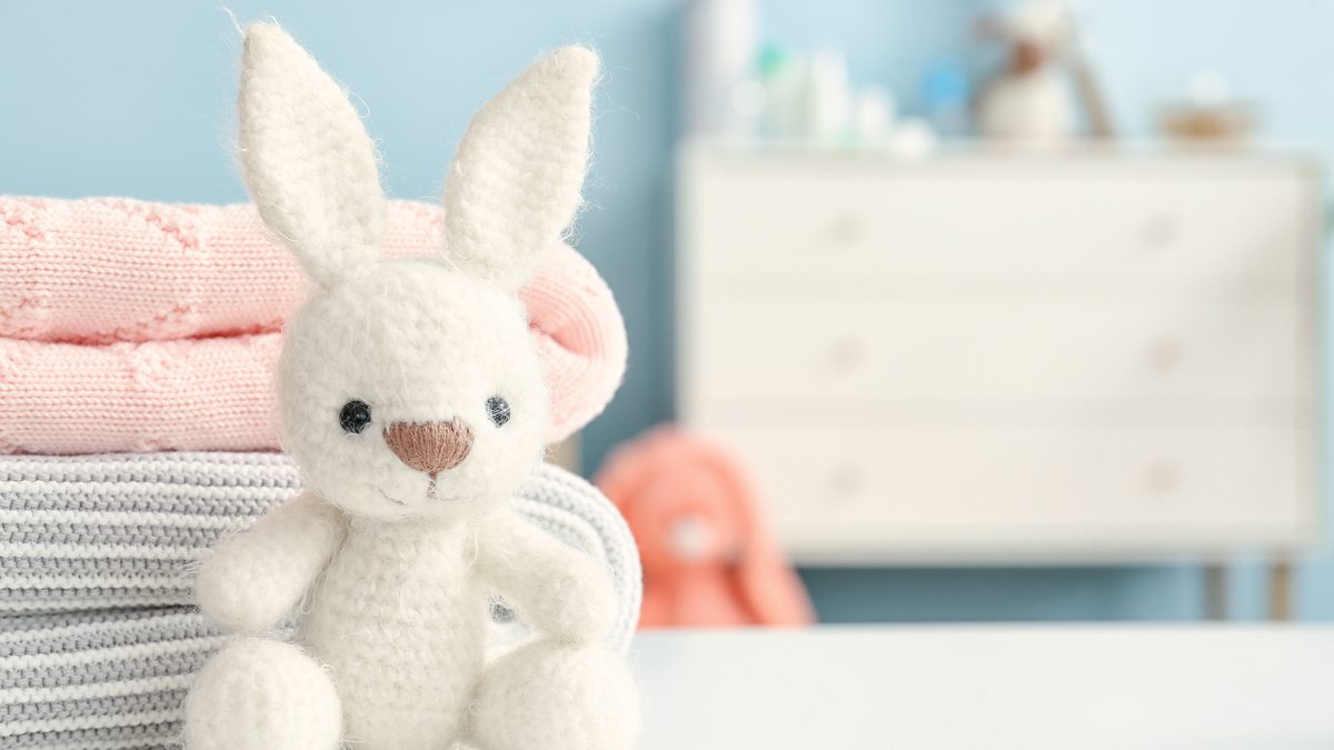 Doudou lapin pos&eacute; sur une pile de v&ecirc;tements d'enfant pli&eacute;s dans une chambre