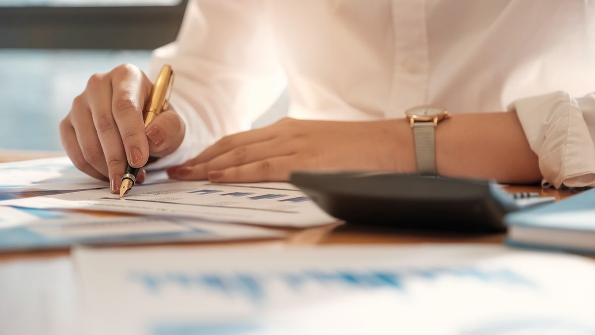 Femme en chemisier calculant des chiffres à l'aide d'une calculatrice devant des documents financiers