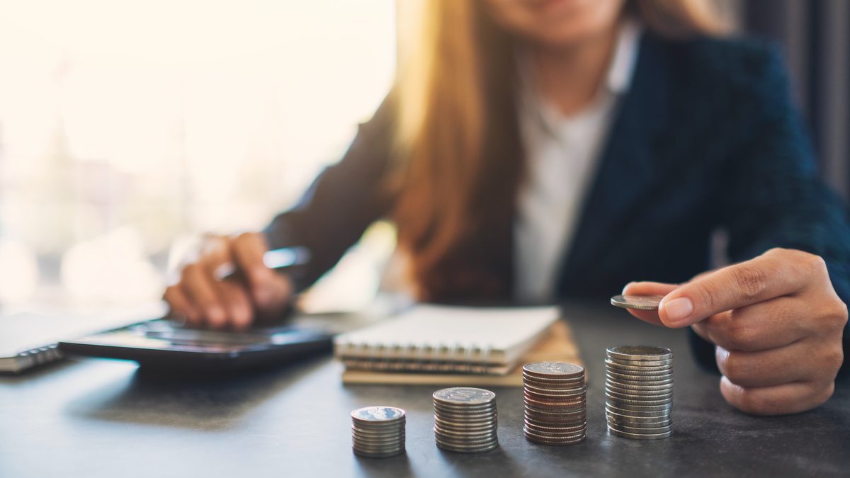 Mains d'une femme empilant des pièces de monnaie à côté d'une calculatrice et d'un carnet, sur une table claire