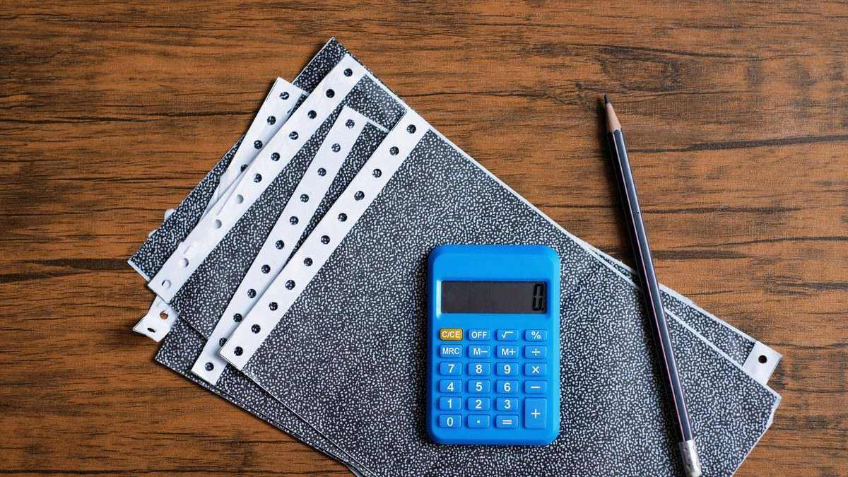 Bulletins de salaire, calculatrice et crayon posés sur un bureau en bois