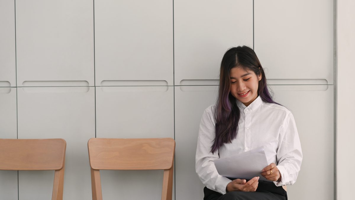 Jeune femme assise dans un couloir, son CV à la main, attendant un entretien d'embauche