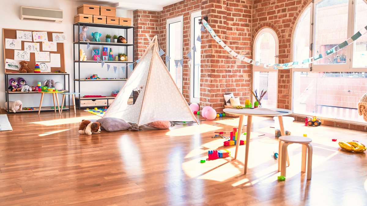 Salle de jeux lumineuse d'une structure petite enfance, avec un tipi, de petites tables et des jouets posés sur un parquet clair