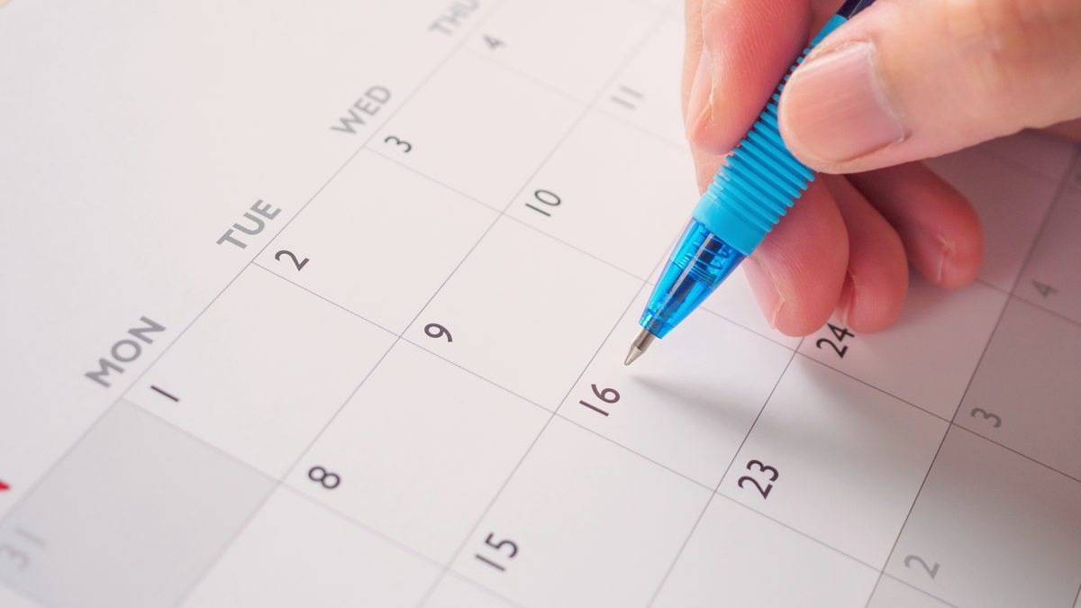 Main tenant un stylo au-dessus d'un calendrier mensuel, pour organiser ses jours de travail