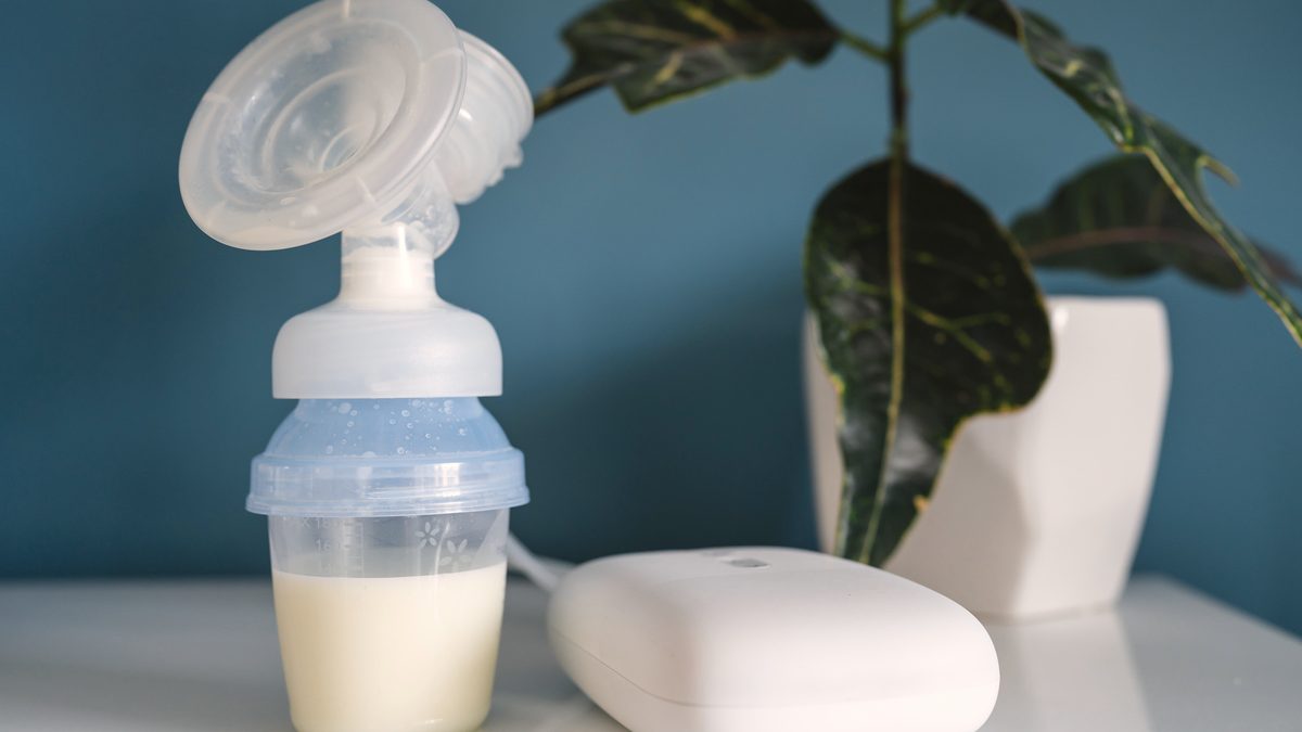 Un tire-lait électrique posé sur une table, avec un biberon rempli de lait maternel et une plante verte en arrière-plan