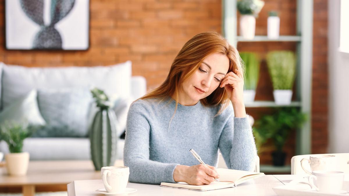 Femme adulte assise à une table claire, en train d'écrire dans un carnet