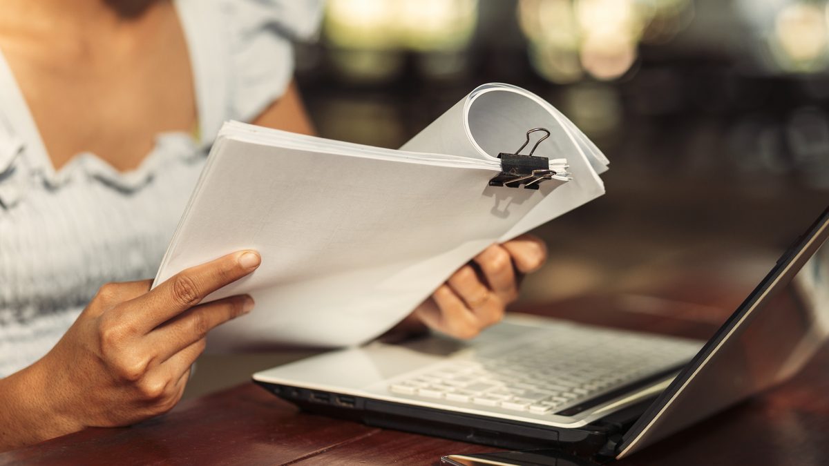 Mains d'une femme lisant attentivement un document administratif à côté d'un ordinateur portable