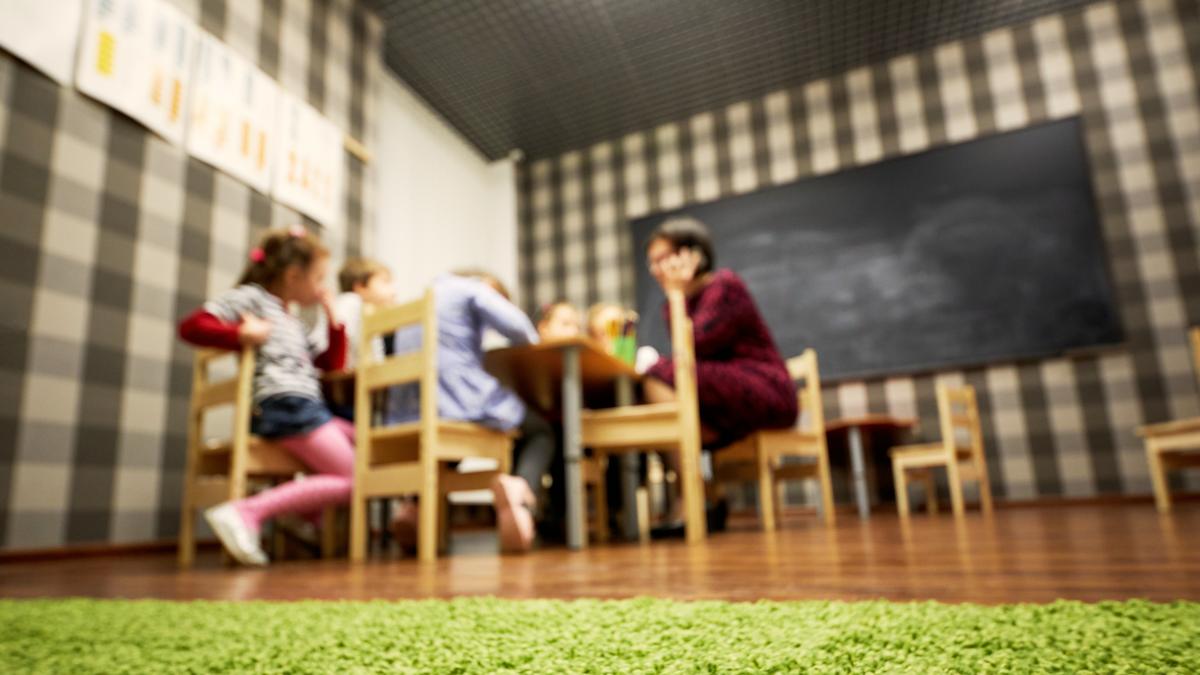 Salle d'accueil collectif avec tables et chaises à hauteur d'enfant, un groupe et une professionnelle en arrière-plan