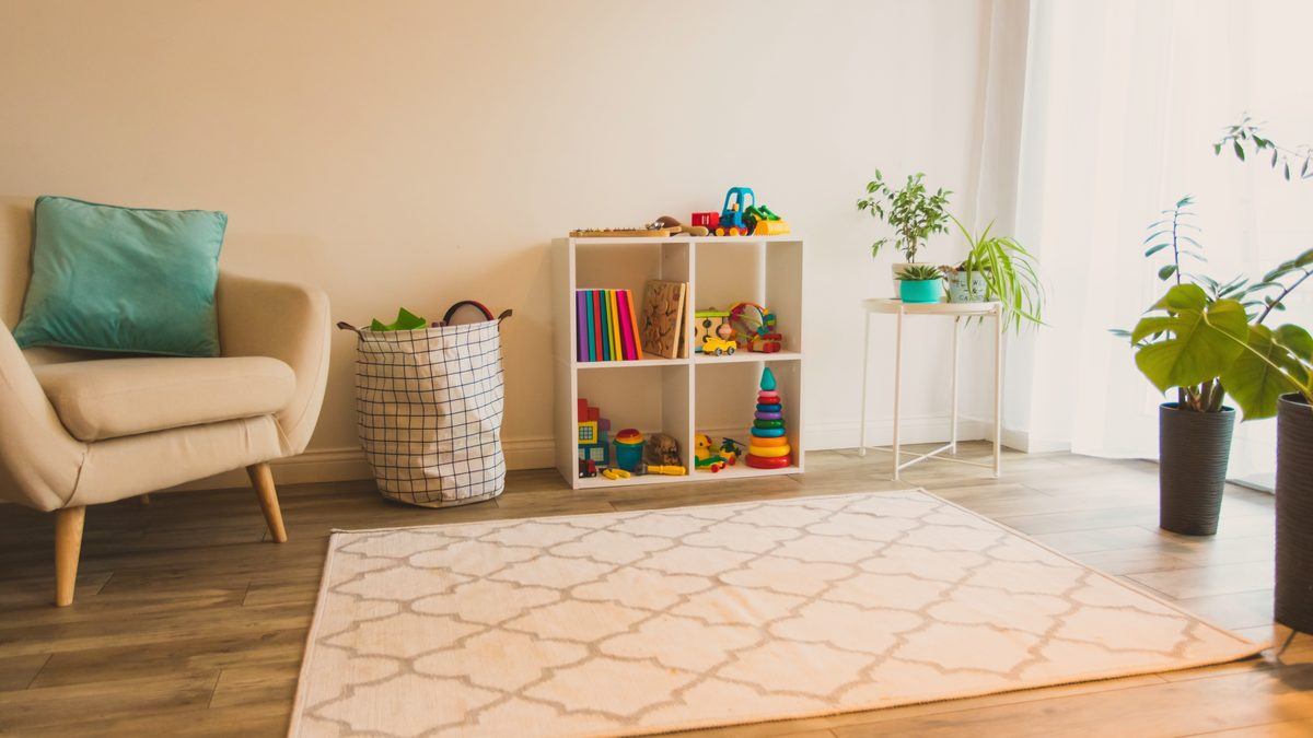 Espace de jeu d'une structure d'accueil de jeunes enfants : étagère de jouets, fauteuil et tapis clair